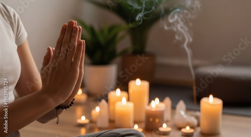 Person meditating with hands clasped, surrounded by numerous lit candles, crystals, and burning incense creating a serene atmosphere.