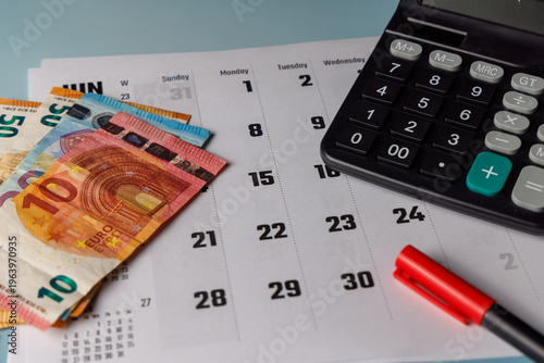 Foto Close up of a calendar near Euro banknotes and office tools illuminated by soft window sunlight on a modern wooden desk for business