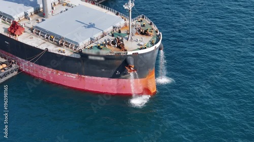 large cargo ship's bow discharging ballast water into the ocean. Maritime engineering operations, industrial shipping logistics, and environmental maintenance at sea.