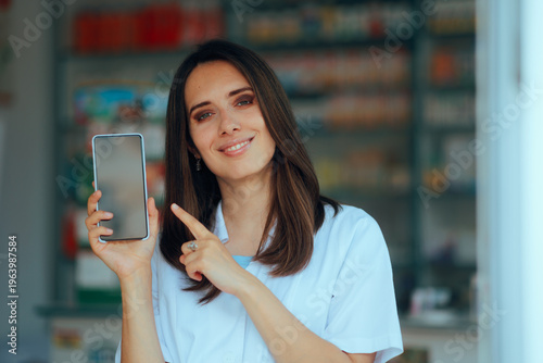 Smiling Pharmacist In Uniform Pointing Finger At a Phone Display. uhappy pharmacy professional assistant showing a mobile phone
