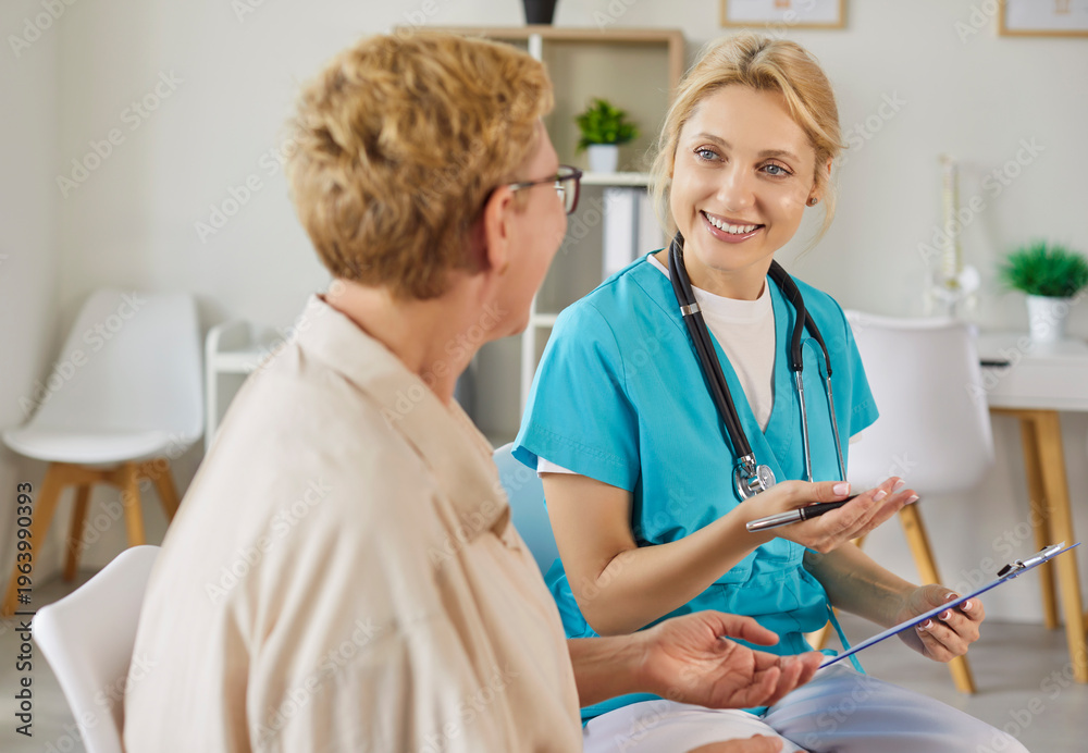 Obraz premium Conversation of smiling nurse and happy elderly patient in modern clinic. Medical consulting of doctor with stethoscope and clipboard during appointment, professional healthcare examination