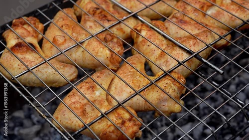 Delicious chicken frying on barbecue grill grate outdoor. Seasoning falling on fresh grilled chicken wings. Summer party food ideas. BBQ Juicy roasting chicken grill legs on grill grate 