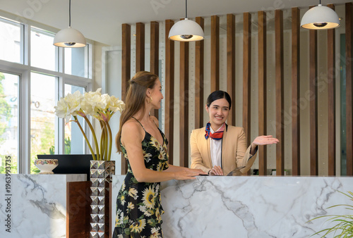 Obraz na plátně Asian hotel receptionist assisting female guest at luxury front desk during chec