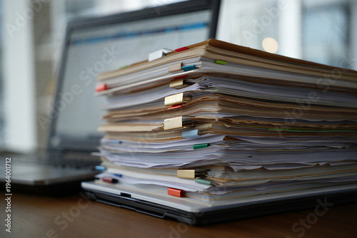 A stack of paperwork and documents on a laptop keyboard in a modern office setting