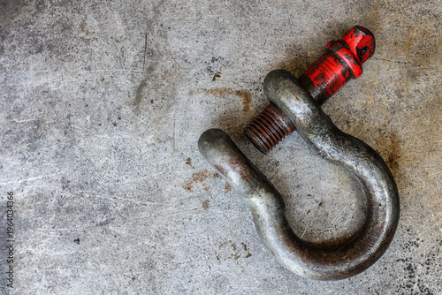 Obraz na płótnie ​A heavy-duty, worn, and rusted industrial screw-pin anchor shackle with a partially faded red-painted pin rests on a scratched metal workshop floor, capturing a detailed texture and rugged feel