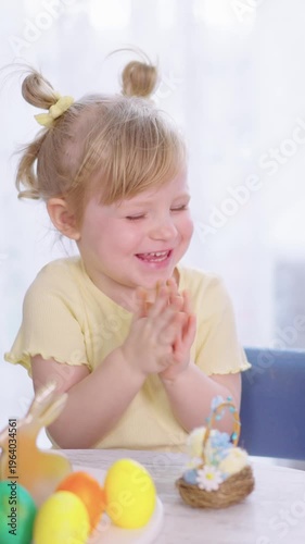 Child smiles while holding a decorated Easter egg. Bright yellow shirt suits the festive atmosphere. Colorful eggs sit nearby, inviting joy and celebration. Soft light enhances the tender