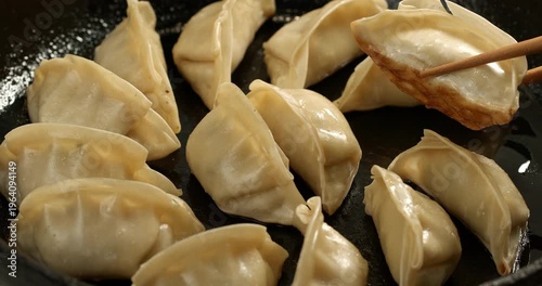 Process of preparing Japanese gyoza dumplings, using chopsticks to take the gyoza to check the frying.