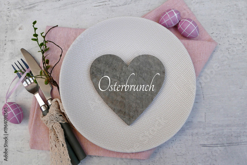 Osterbrunch Gedeck für Gastronomie und Catering-Marketing – Gedeckter Tisch mit Schriftzug Osterbrunch auf einem Herz auf rosa Stoffserviette, daneben Besteck mit Spitzenband und dekorative Ostereier,