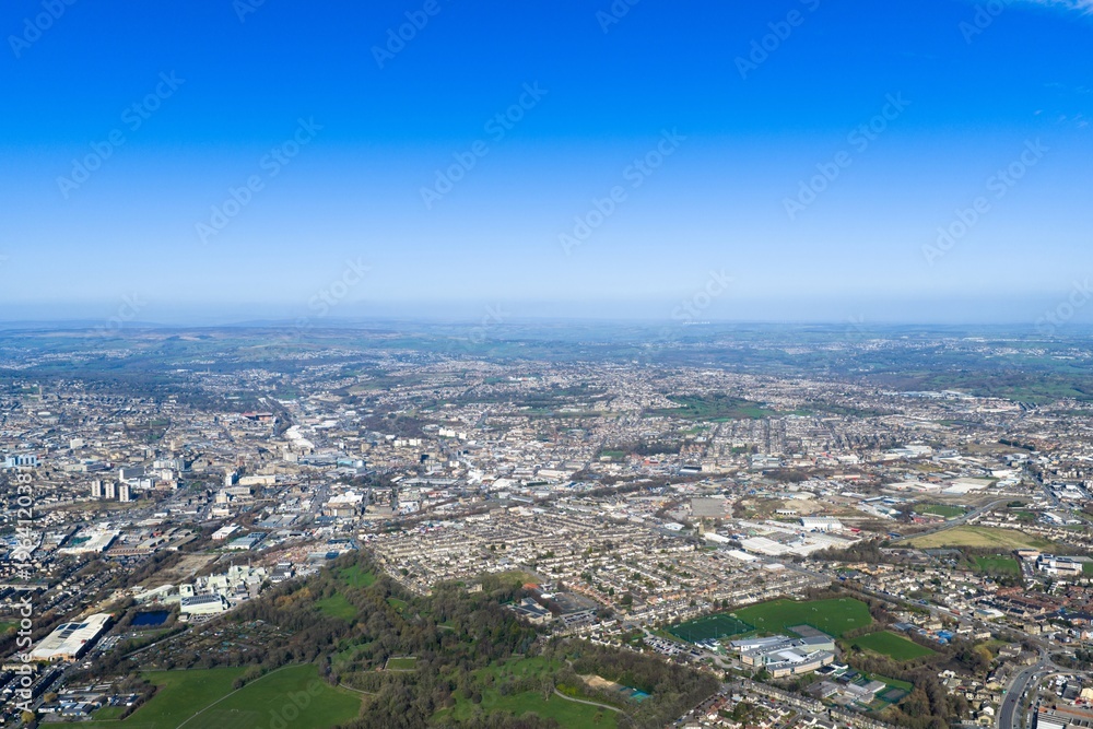 Obraz premium Wide aerial view of the city of Bradford West Yorkshire UK showing urban housing industrial estates and green spaces across rolling terrain captured from a high vantage point in clear daylight