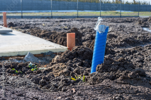 Blue corrugated conduit pipe emerging from soil at construction site, underground utility installation near building foundation, infrastructure and drainage system concept.