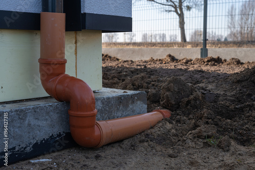 PVC sewer pipe connected to house downspout drainage at building foundation, outdoor rainwater drainage system installation.