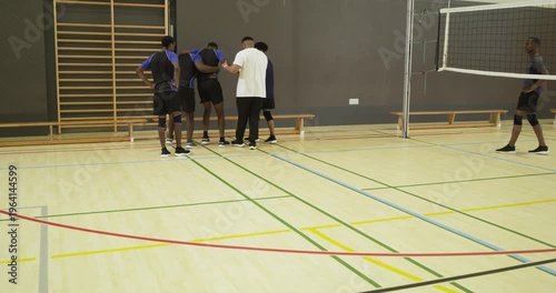 Diverse male volleyball players supporting limping teammate toward bench, crouching inspecting shoe