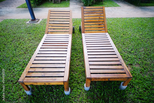 Brown wooden beach chairs on green grass in tropical garden