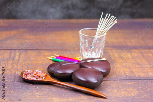 Still life of acupuncture needles in glass with spa stones and herbal salt on wooden table, traditional Chinese medicine and wellness concept.