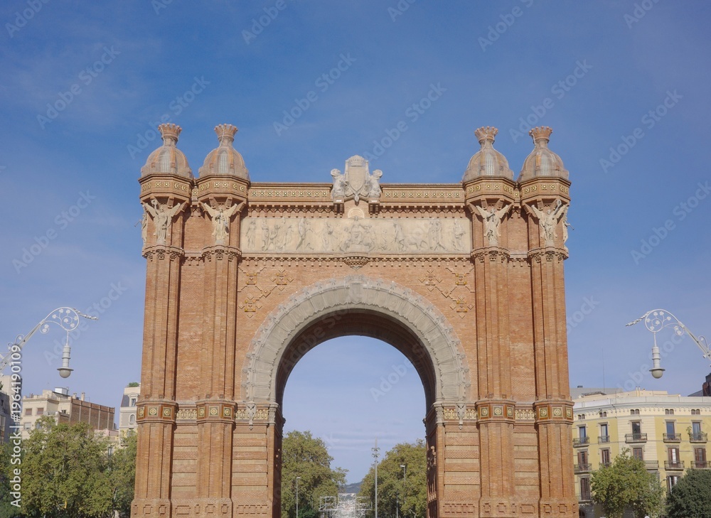 Fototapeta premium Iconic Arc de Triomf Triumphal Arch with Ornate Red Brick Facade and Decorative Sculptures Against Clear Blue Sky in Barcelona, Spain