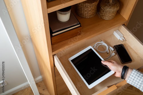 Digital detox with man hand putting tablet and phone into drawer at home. Time limit in using gadgets, offline from social media and internet, lifestyle balance and mental health concept.