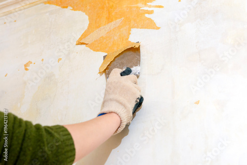 A woman is tearing old wallpaper off the wall.