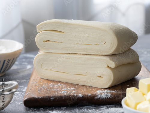A pile of uncooked puff pastry dough, also known as pâte feuilletée in French. It's composed with dough and butter folding in a dough, with flour and butter in scene.