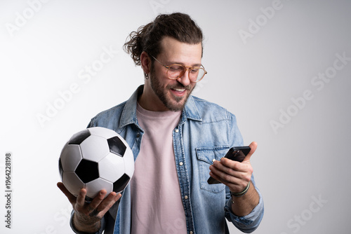 Fotografie positive man holding soccer ball and messaging on mobile phone isolated on grey, banner