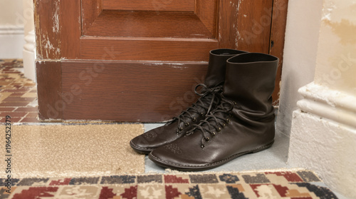 Dark Brown Leather Boots with Laces Resting by Worn Wooden Door