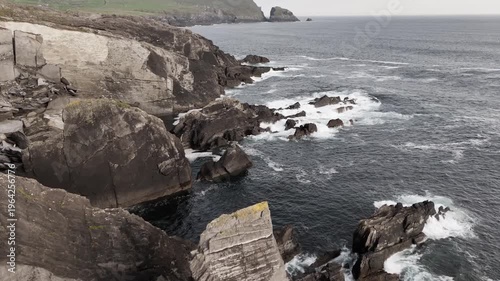 Dramatic waves crash against dark, jagged rocks along a dramatic coastline.