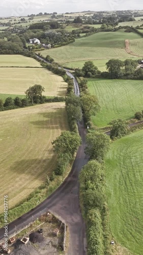 Drone perspective above the rolling green hills and traditional hedgerows of rural Ireland with farm buildings and vehicles.