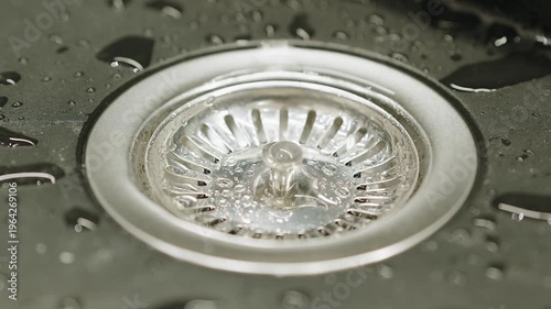Close-Up Of Stainless Steel Sink Drain With Running Water And Water Droplets