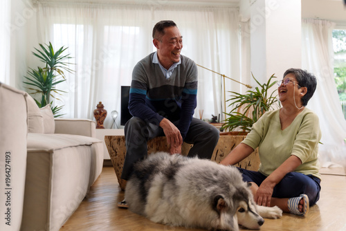 A senior man and woman are petting a large dog in a living room