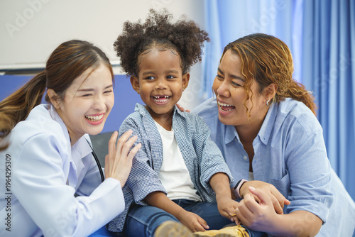 The little girl in curly hair is sitting on the bed in the hospital. The doctor is examining and check the child's health.
