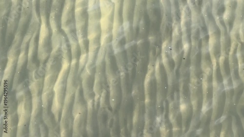 abstract close-up of wave-formed sand ripple patterns seen through crystal-clear shallow coastal water
