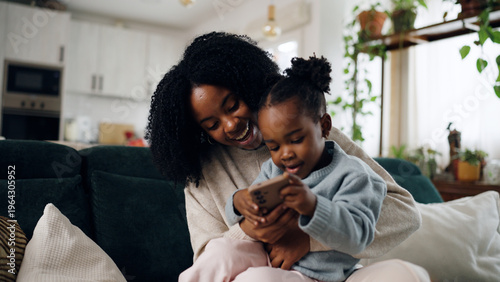 Photos African American mother and daughter sitting on sofa, laughing and bonding while