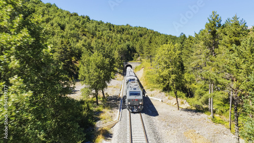 Φωτογραφία Freight train traveling on railroad tracks, entering a tunnel in a lush green mo