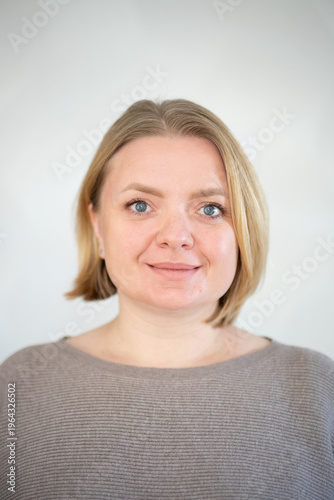 Smiling caucasian woman with blonde short hair looking at camera, close-up portrait, positive expression, adult person, genuine smile, neutral light background