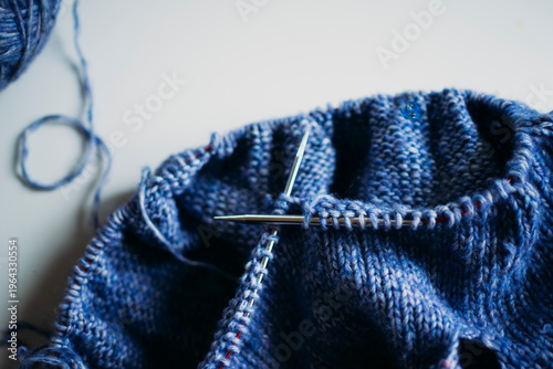 Close-up of metal knitting needles crossed in blue wool fabric, detailed texture of knitwear, darker background, creating handmade clothes concept