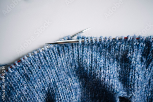 Macro shot of blue knitted stitches on metal needles, detailed texture of wool fabric, soft natural light, close-up of handicraft process