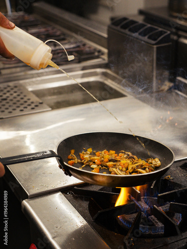 Принти на полотні Chef pouring oil into frying pan while cooking vegetables on stove, professional