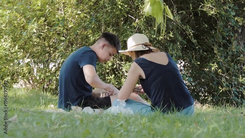 Young Man and Woman Assembling a Wooden Model Puzzle Together Outdoors in a Green Park on a Sunny Day