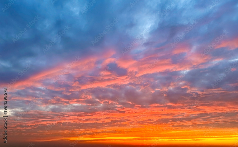 Obraz premium Stunning sunset sky filled with textured clouds glowing in shades of orange, pink, and blue, creating a dramatic and colorful natural background.