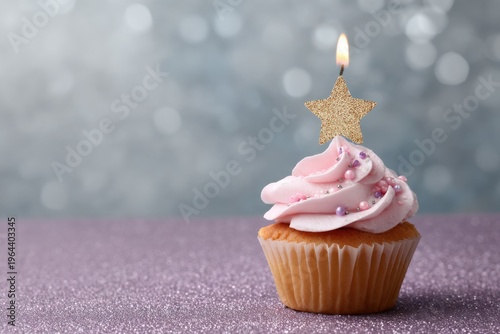 Pink cupcake with star candle on glittery surface and sparkling bokeh background