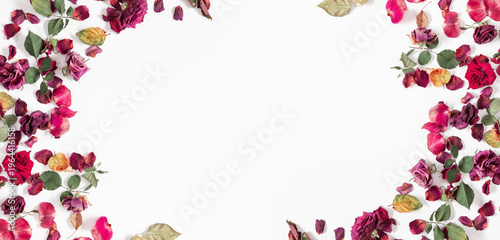 Floral frame made of dried red pink rose flowers, petals and green leaves on white background. Flat lay, top view. Romantic elegant composition with copy space for text. Banner, header template