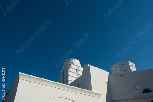 Abstract geometric detail of a white modern building facade with circular windows against a deep blue clear sky.