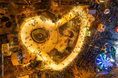Aerial drone view of a festive ice skating rink at a Christmas market at night.