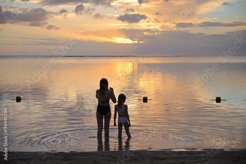 mom and daughter taking photo of sunset on the beach