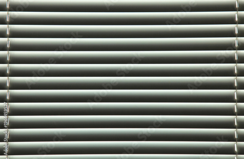 Linear background of lowered blinds in a living space in soft color. Closed blinds, texture, backdrop. Aluminum strips of thin blinds on window. Window blind surface in yellowish light and shadow