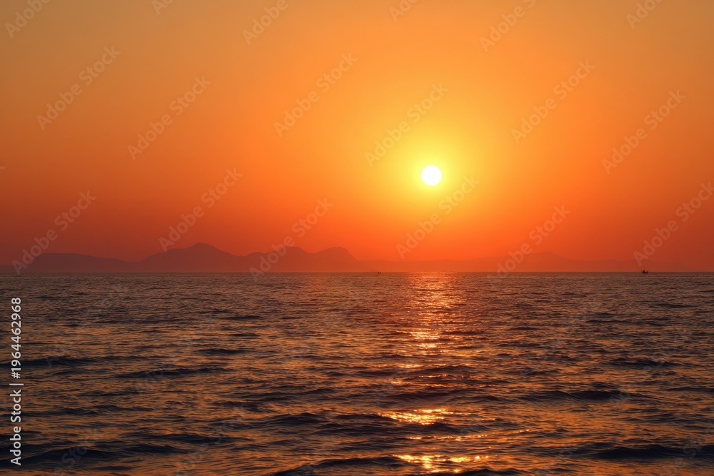 Fototapeta premium Vibrant orange sunset over calm ocean waves with distant mountains