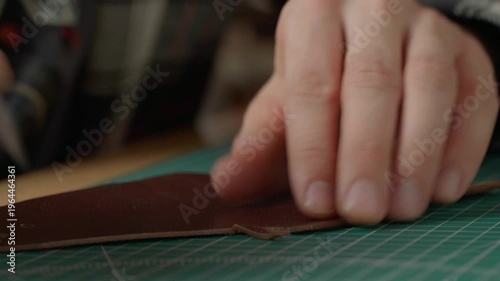 Close-up of a hand with a sharp leather cutting knife trimming or cutting a piece of natural brown leather. Fabrication technique.