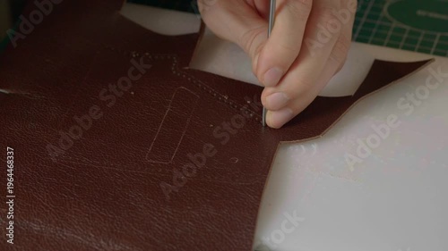 A close-up cinematic shot showing a leather craftsman using a small metal hammer and a round punch to create a series of perfect holes in a strip of natural brown leather.