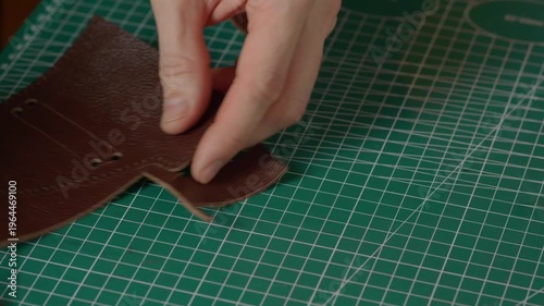 Close-up of a hand with a sharp leather cutting knife trimming or cutting a piece of natural brown leather. Fabrication technique.
