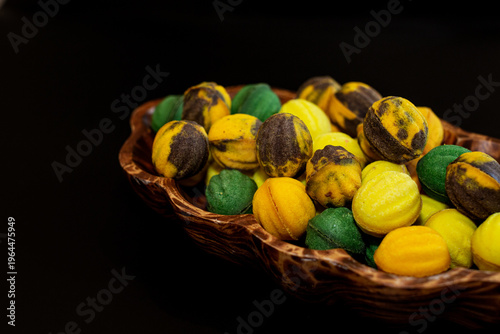 Multicolored nut-shaped cookies with filling on a wooden tray on a black background