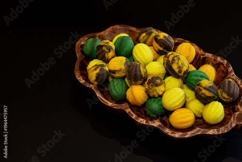 Multicolored nut-shaped cookies with filling on a wooden tray on a black background